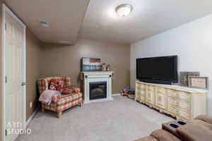 Living room with light colored carpet, a glass covered fireplace, and a textured ceiling