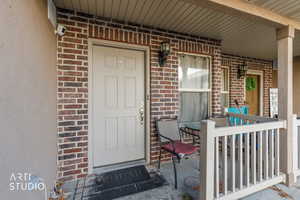 View of exterior entry featuring brick siding and covered porch