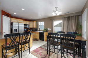 Kitchen featuring a breakfast bar, light brown cabinets, black appliances, a chandelier, and pendant lighting