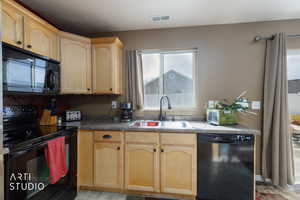 Kitchen with light brown cabinetry, black appliances, and dark countertops