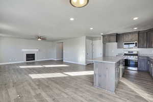Kitchen with appliances with stainless steel finishes, a kitchen island, a glass covered fireplace, light stone countertops, and light wood finished floors