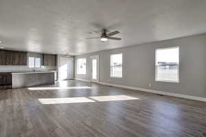 Unfurnished living room with ceiling fan, a textured ceiling, and dark wood-style flooring