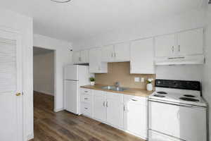 Kitchen with white appliances, white cabinets, light countertops, under cabinet range hood, and dark wood finished floors