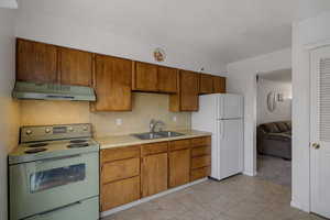 Kitchen with electric range oven, freestanding refrigerator, light countertops, under cabinet range hood, and brown cabinets