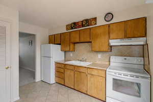 Kitchen with white appliances, light countertops, under cabinet range hood, and brown cabinetry