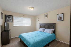 Carpeted bedroom featuring a textured ceiling and baseboards
