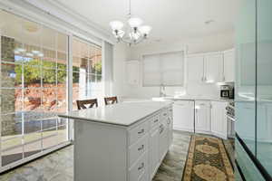 Kitchen with white cabinets, decorative light fixtures, light countertops, dishwasher, and a center island