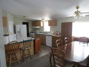Kitchen featuring white appliances, a breakfast bar, ceiling fan, lofted ceiling, and a peninsula