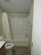 Full bathroom with shower / bath combo with shower curtain, vanity, dark tile patterned floors, and a textured ceiling