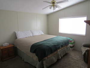 Bedroom with dark colored carpet, ceiling fan, and lofted ceiling