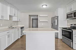 Kitchen featuring appliances with stainless steel finishes, white cabinets, a kitchen island, dark wood-type flooring, and a textured ceiling