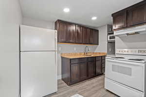 Kitchen with dark brown cabinets, white appliances, under cabinet range hood, light stone countertops, and recessed lighting