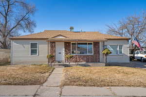 Bungalow-style home with a chimney, a porch, stone siding, and a shingled roof