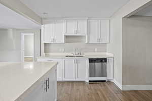 Kitchen featuring white cabinets, dishwasher, a textured ceiling, light wood-style flooring, and light stone counters