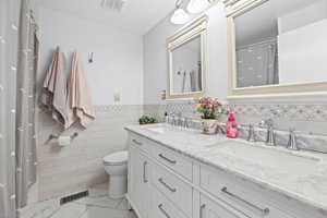 Full bathroom with double vanity, tile walls, wainscoting, and a shower with curtain