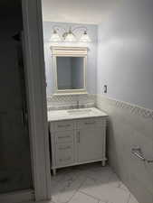 Bathroom featuring vanity, tile walls, wainscoting, a stall shower, and light marble finish flooring