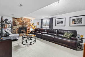 Living room featuring a textured ceiling, carpet flooring, and a stone fireplace