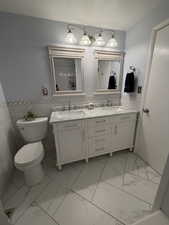 Full bathroom featuring double vanity, tile walls, a wainscoted wall, light marble finish flooring, and a shower