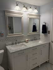 Full bath with double vanity, wainscoting, and tile walls
