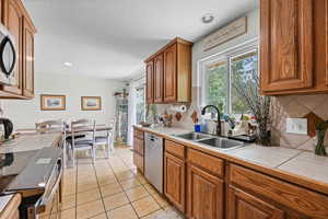 Kitchen with wood finish cabinetry, stainless steel appliances, tile counters, light tile patterned floors, and recessed lighting
