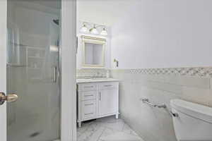Bathroom featuring vanity, a stall shower, a wainscoted wall, and tile walls
