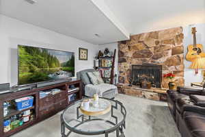 Living area featuring a stone fireplace, carpet floors, and a textured ceiling