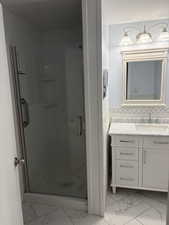 Full bath with a stall shower, vanity, and light marble finish flooring
