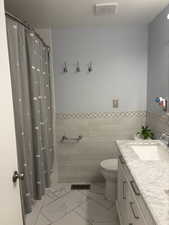 Bathroom featuring vanity, tile walls, curtained shower, and a wainscoted wall