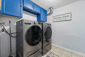 Laundry area with light tile patterned flooring, washing machine and clothes dryer, a textured ceiling, and cabinet space