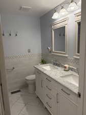 Full bath with double vanity, a wainscoted wall, and tile walls