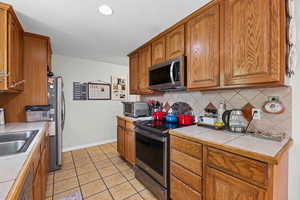 Kitchen featuring stainless steel appliances, wood finish cabinetry, light tile patterned floors, tile counters, and backsplash