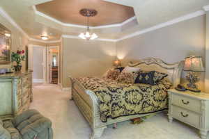 Bedroom featuring a tray ceiling, crown molding, light colored carpet, and a chandelier