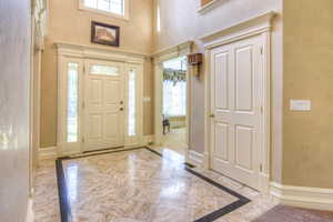 Foyer with light marble finish flooring, inlaid floor details, and a towering ceiling