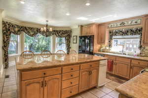 Kitchen with backsplash, light stone countertops, black fridge with ice dispenser, ornamental molding, and recessed lighting