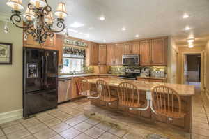 Kitchen featuring stainless steel appliances, light stone countertops, pendant lighting, brown cabinets, and light tile patterned floors