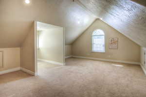 Bonus room with lofted ceiling, light carpet, and a textured ceiling