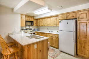 Kitchen featuring light countertops, white appliances, a breakfast bar area, a textured ceiling, and a peninsula