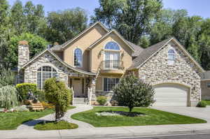 View of front of property with stone siding, a balcony, concrete driveway, a front lawn, and a garage
