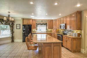 Kitchen featuring light stone countertops, stainless steel appliances, brown cabinets, light tile patterned floors, and decorative backsplash