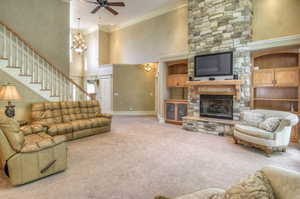 Living area with a high ceiling, ornamental molding, a fireplace, carpet flooring, and ceiling fan