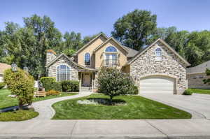 View of front of home with stone siding, driveway, a front yard, a garage, and stucco siding