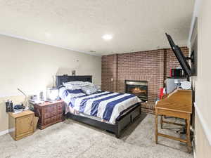 Bedroom with a brick fireplace, light colored carpet, ornamental molding, brick wall, and a textured ceiling
