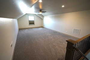 Additional living space with vaulted ceiling, ceiling fan, dark carpet, and a textured ceiling