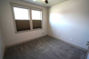 Empty room featuring dark carpet and a ceiling fan