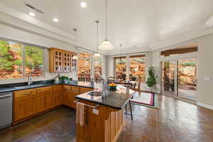 Kitchen with stone tile floors, glass insert cabinets, a breakfast bar area, dark stone countertops, and stainless steel dishwasher