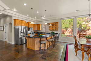 Kitchen featuring stone tile flooring, appliances with stainless steel finishes, a kitchen breakfast bar, brown cabinets, and dark stone countertops