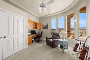Home office featuring ceiling fan, light colored carpet, and built in desk