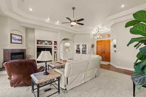 Carpeted living room with arched walkways, a raised ceiling, a fireplace, built in features, and a chandelier