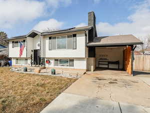 Split foyer home with roof mounted solar panels, a front yard, concrete driveway, a chimney, and brick siding