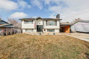 Bi-level home with roof mounted solar panels, a front yard, a chimney, and concrete driveway
